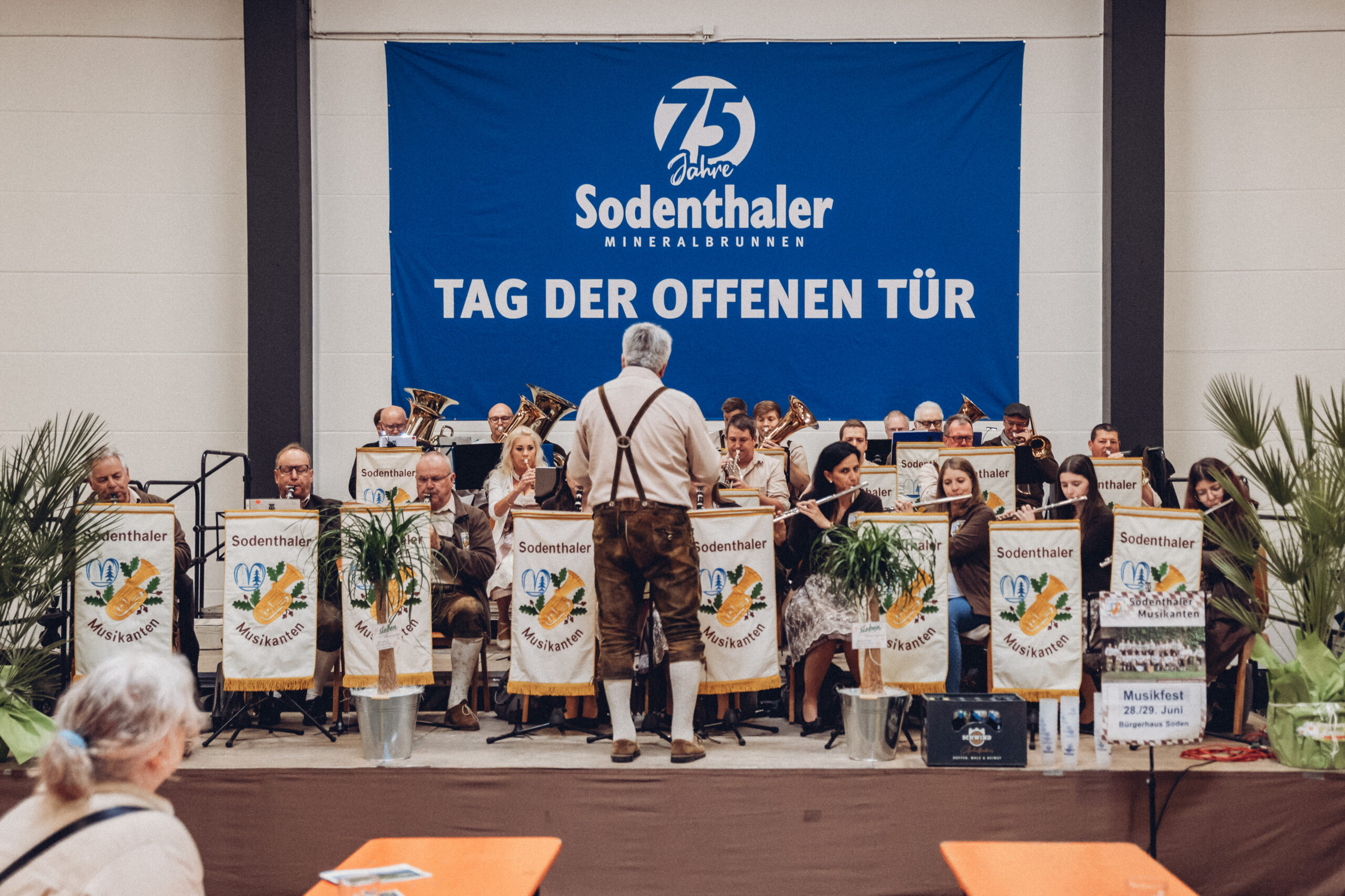 Viele Besucher bewegen sich auf einem Werksgelände. Im Hintergrund sieht man einen Getränkestand und eine Halle mit offenen Toren.