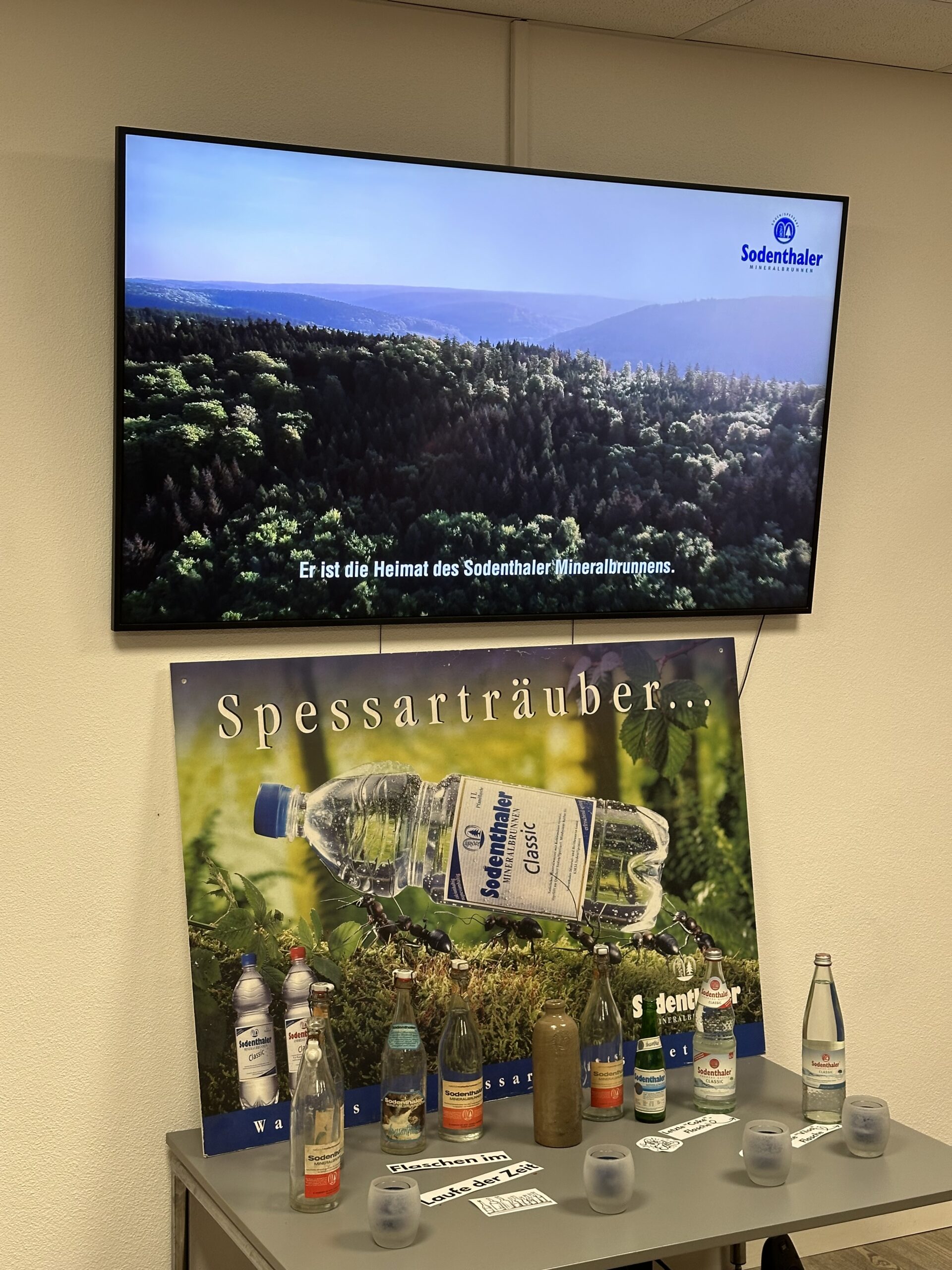Ausstellung über die Geschichte von Sodenthaler mit alten Flaschen und einem Bildschirm, der einen Film über den Spessart zeigt.