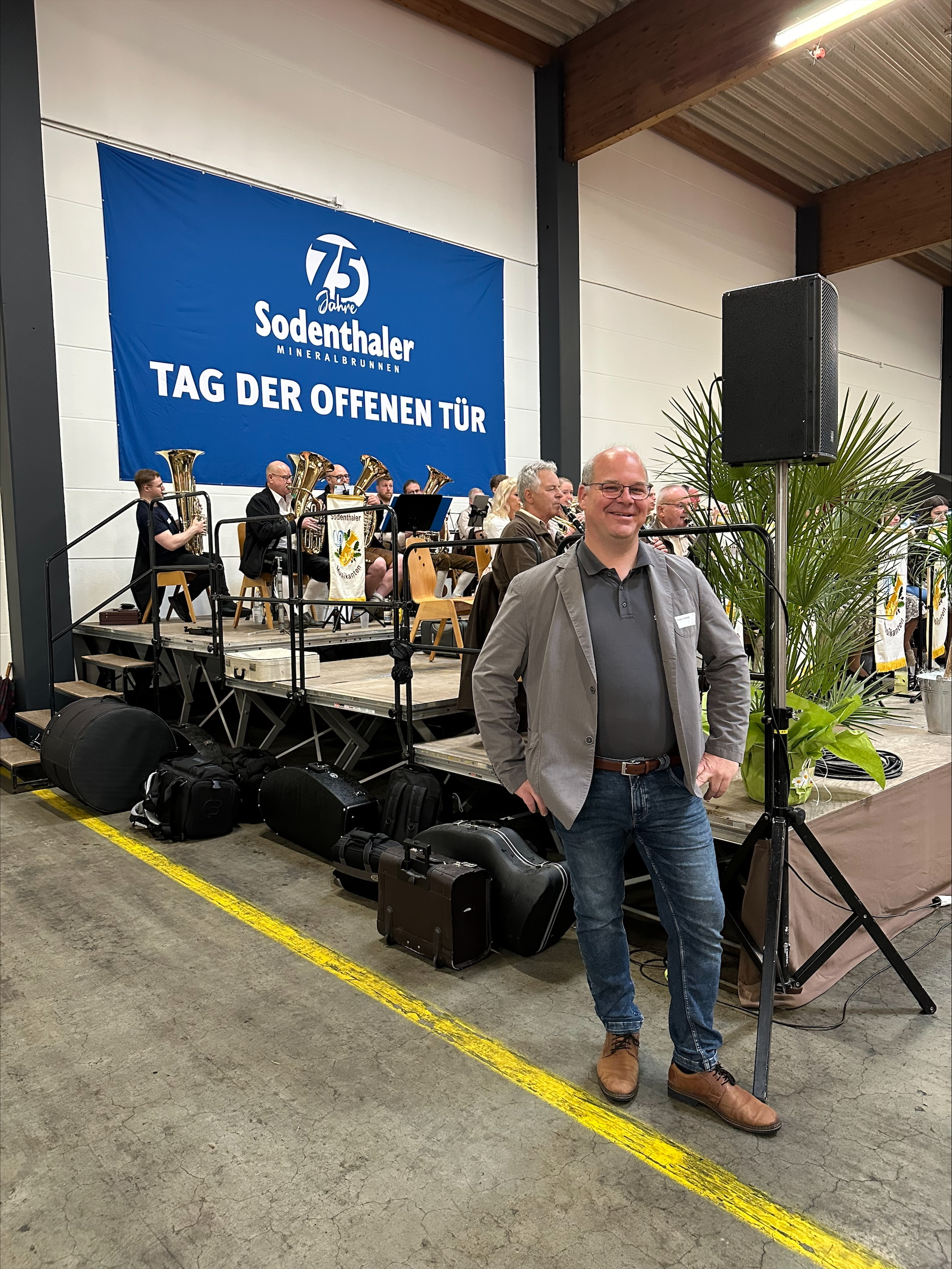 Ein Mann posiert vor einer Bühne mit Blaskapelle beim Tag der offenen Tür von Sodenthaler.