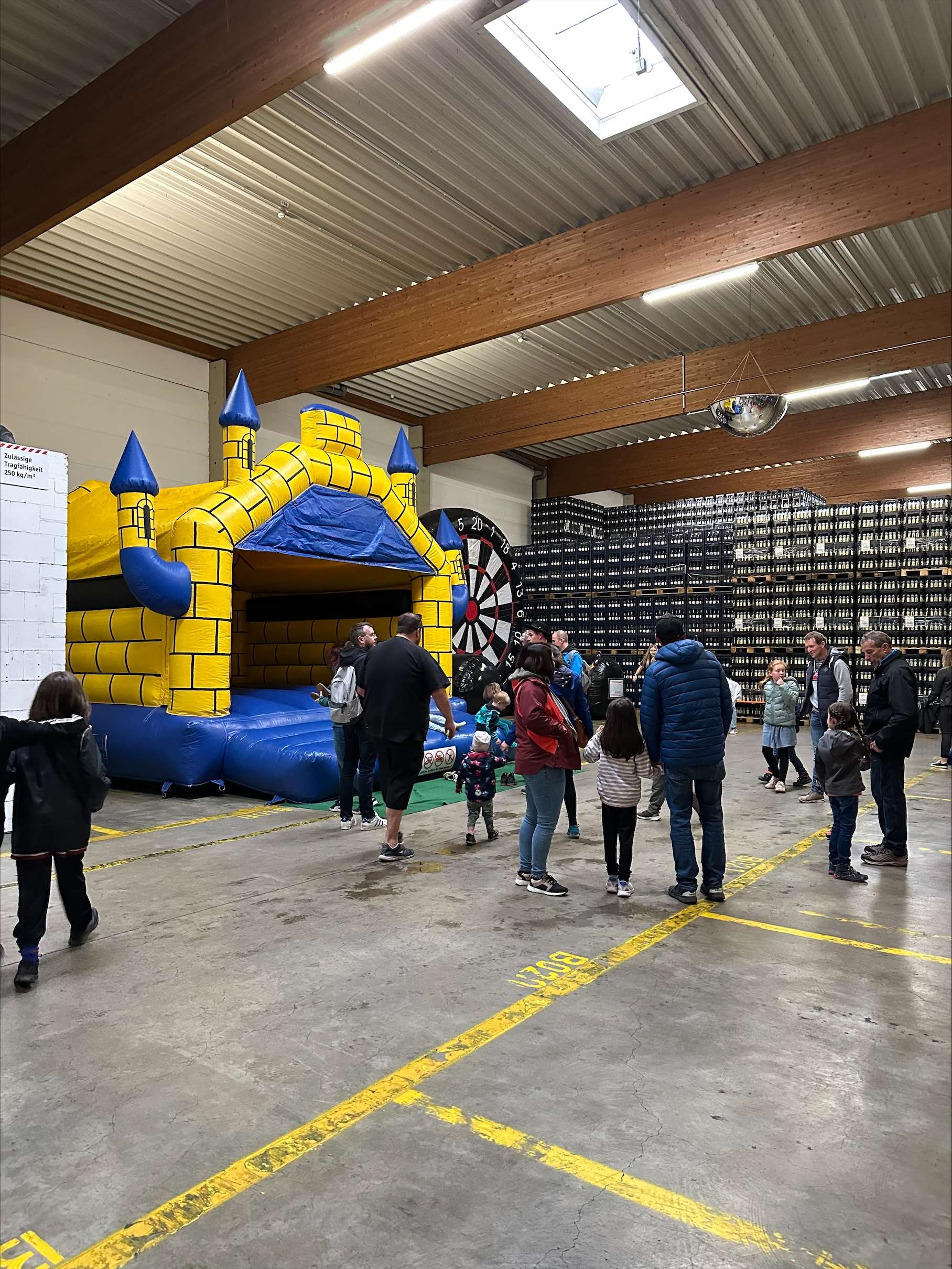 Kinder spielen bei einer gelben Hüpfburg und einem übergroßen Dartspiel in einer Halle.